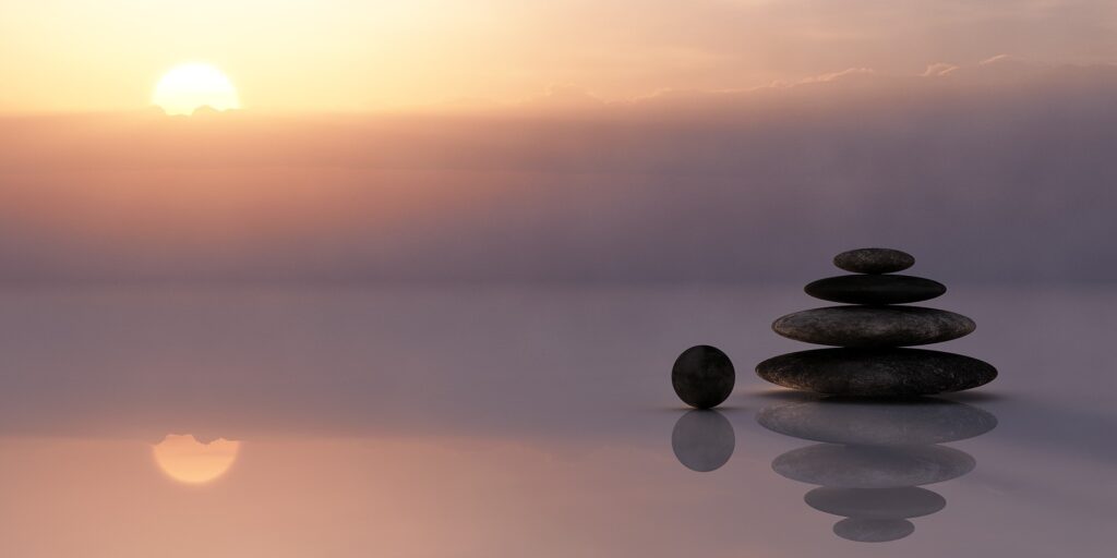 symmetrically stacked flat stones on a reflective surface with setting/rising sun in background