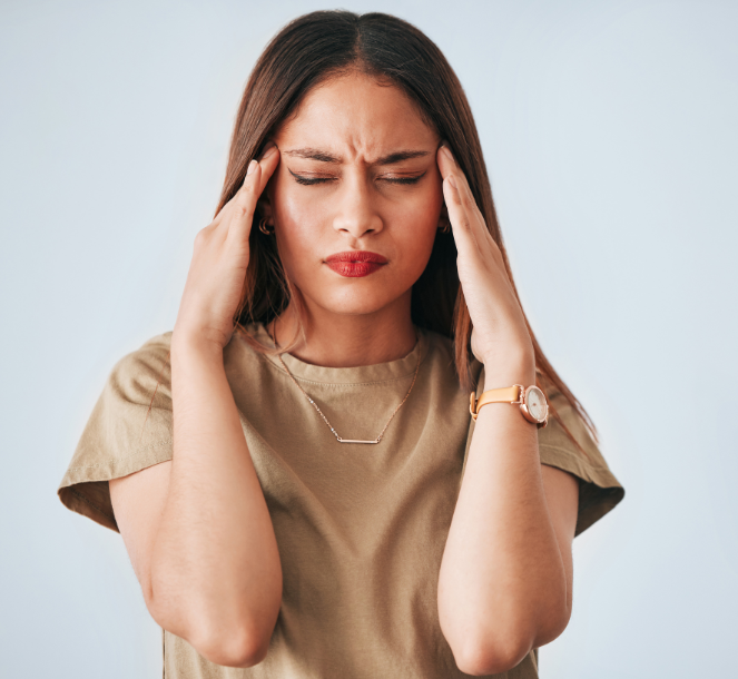 dark haired woman with closed eyes, forehead creased and rubbing her temples to show mental overload when you loose your body awareness practice